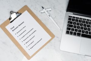 A picture of a clipboard with a checklist of things to do for picking a domain names. The clipboard is on a desk next to a laptop.