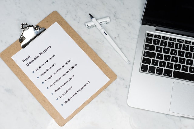 A picture of a clipboard with a checklist of things to do for picking a domain names. The clipboard is on a desk next to a laptop.